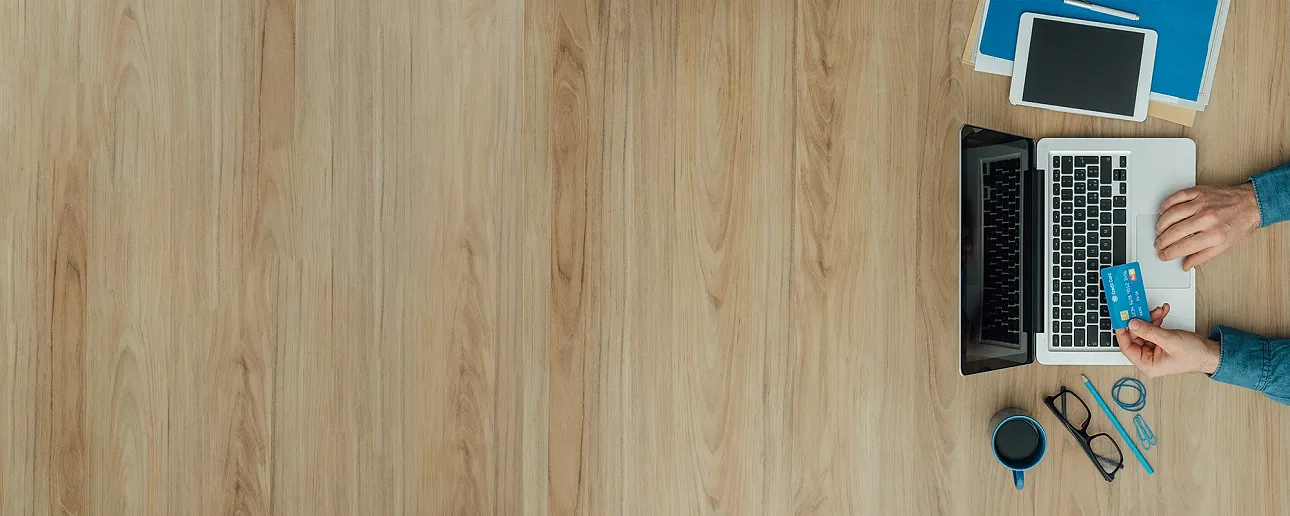 Close-up of a person working at a laptop taken from above with a wood background.