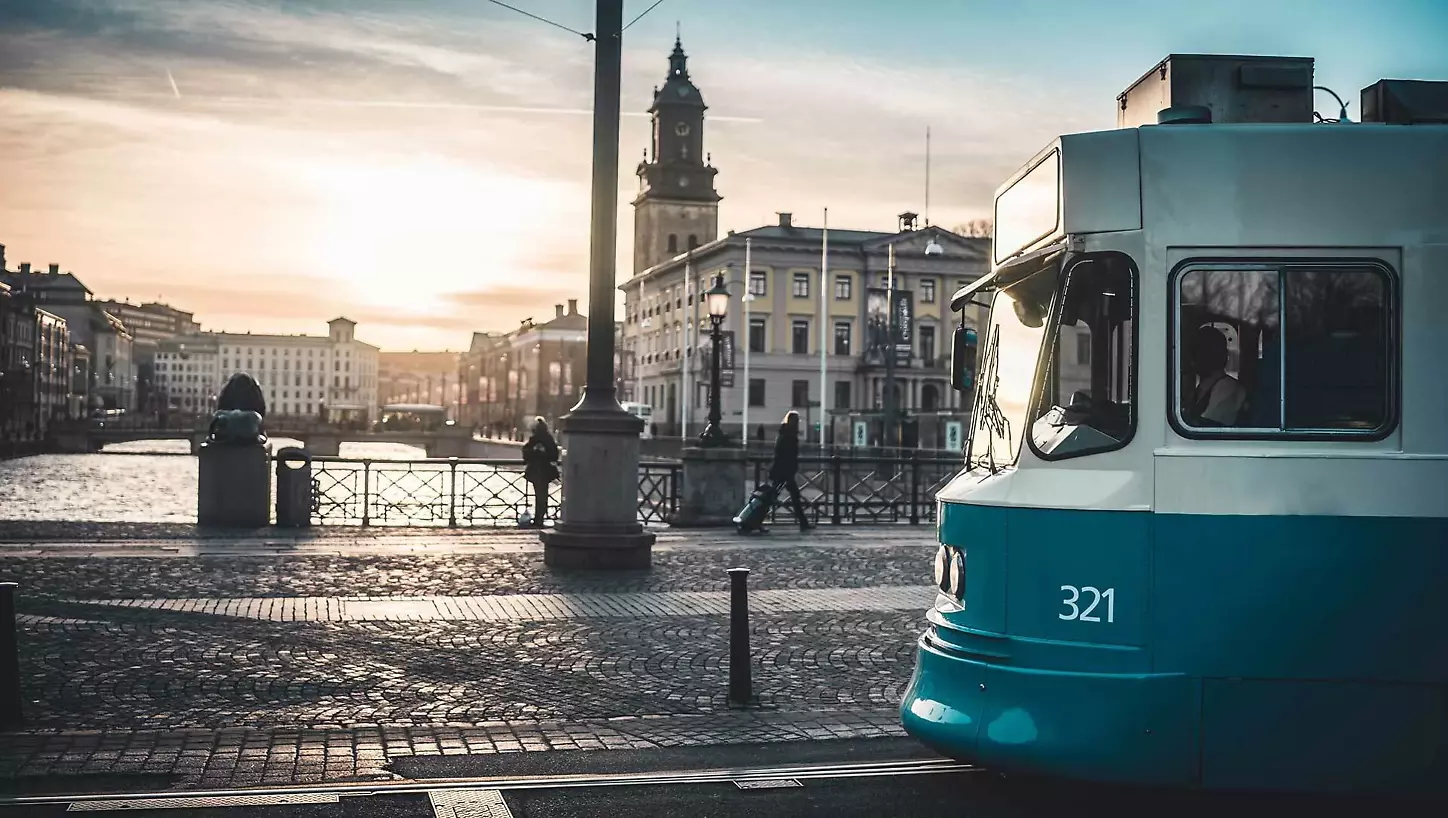 En spårvagn i Göteborg passerar en solig stadsvy med en kyrka i bakgrunden.