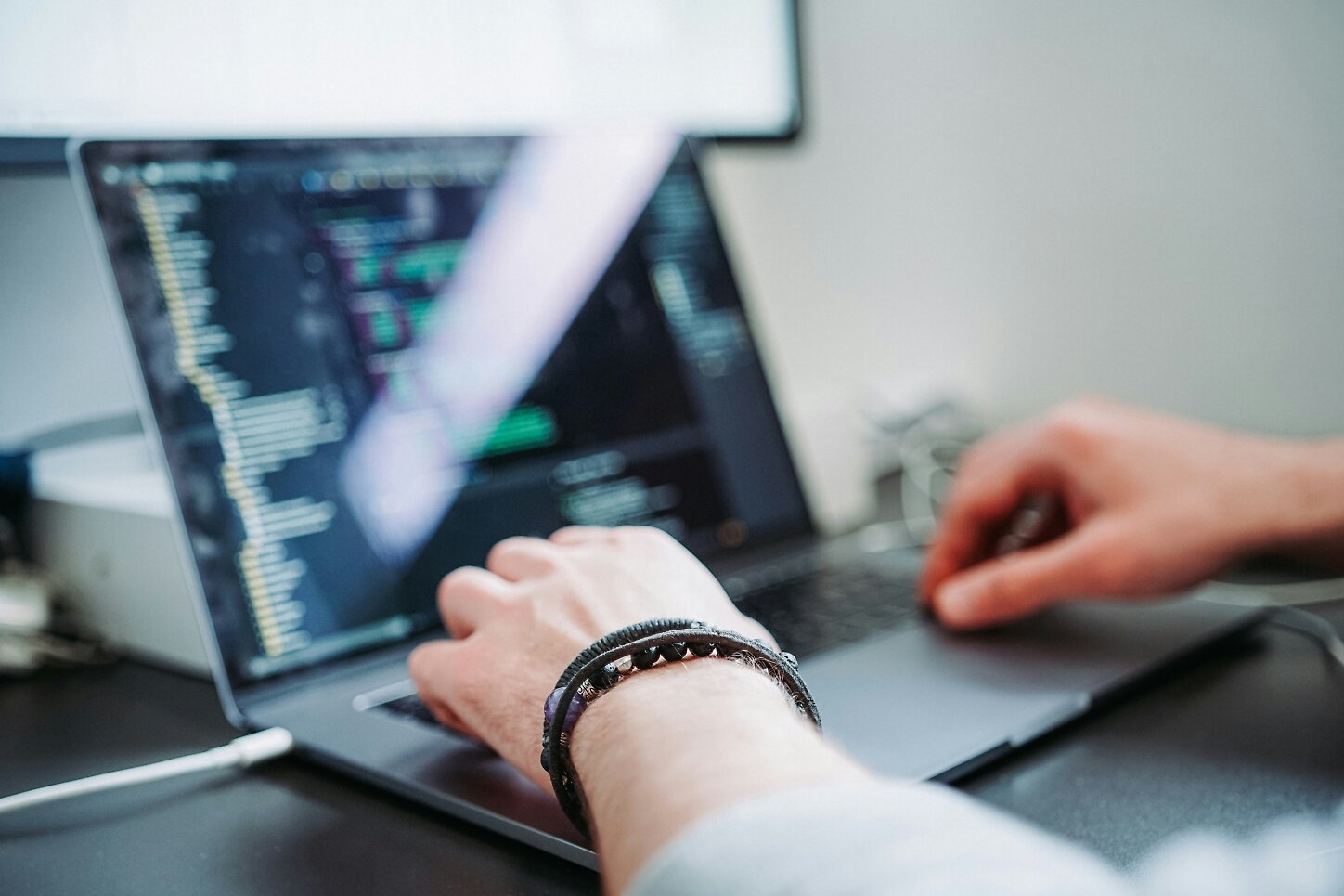 En person arbetar vid en bärbar dator, med händerna vilande på tangentbordet. Datorskärmen visar kod eller programmeringsrelaterad text.