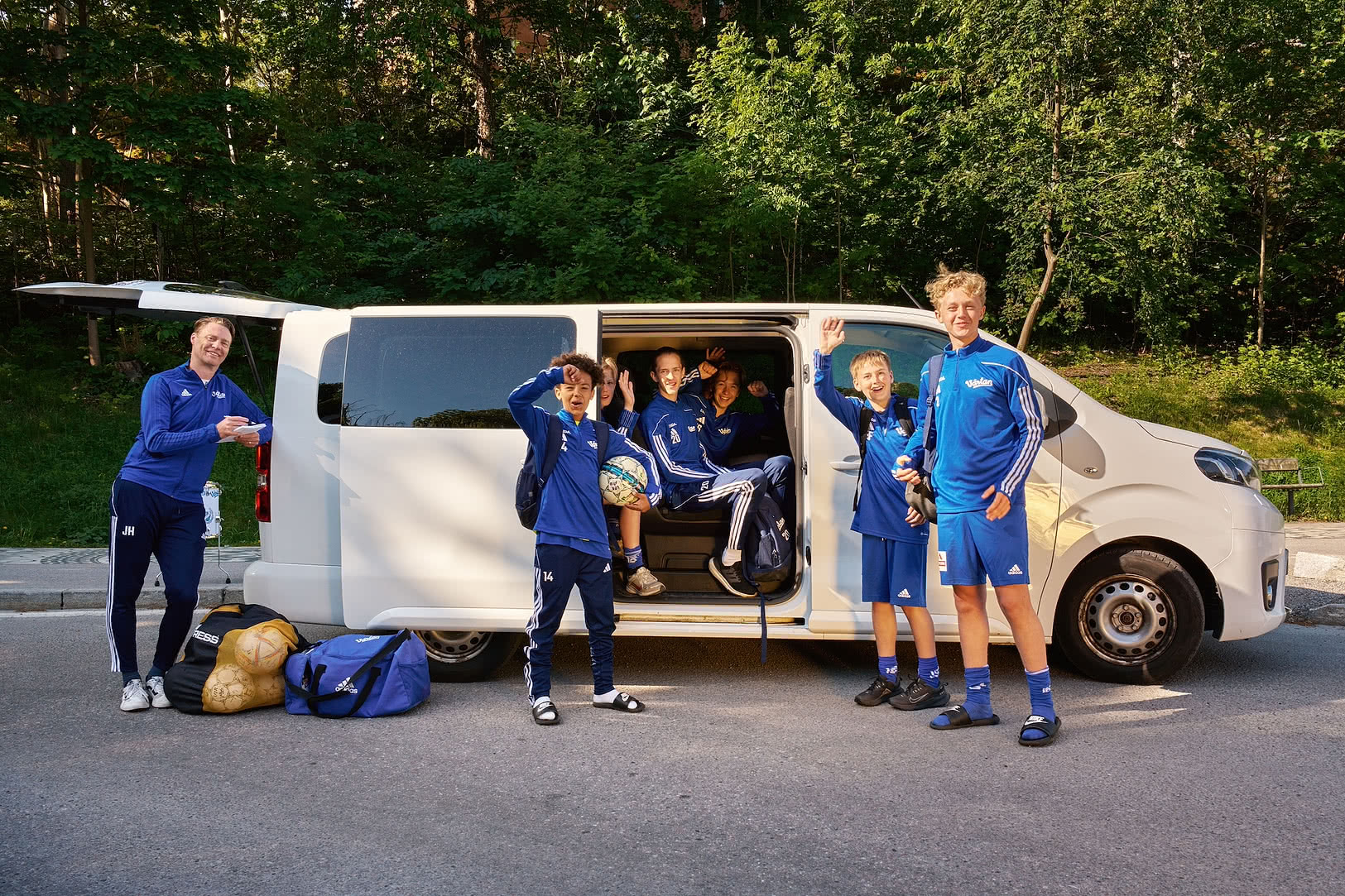 Ett ungdomslag i träningskläder står vid en minibuss inför avfärd till match eller turnering.
