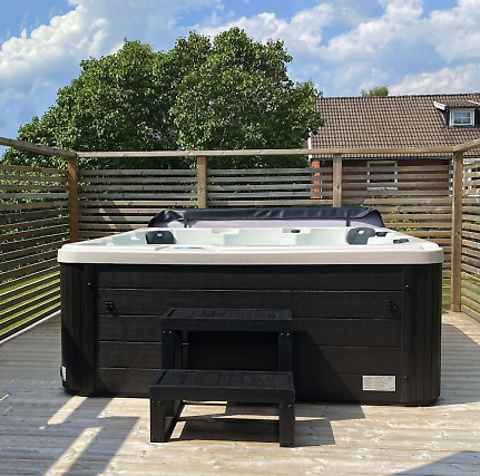 En svart jacuzzi från Outl1 står på en altan ute i solljuset