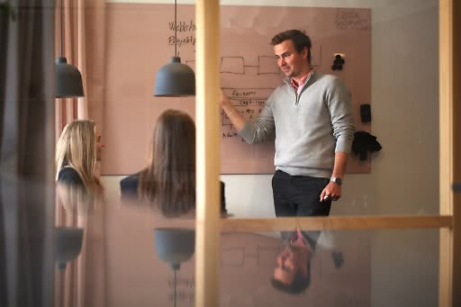 Person leder ett möte vid whiteboard på Webbhuset, förklarar projektflöde för kollegor.